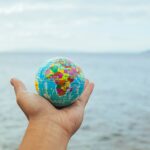 A hand holding a small globe with an ocean backdrop, symbolizing global connection and travel.